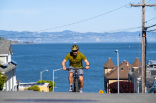 person riding ebike on busy street uphill with ocean in background